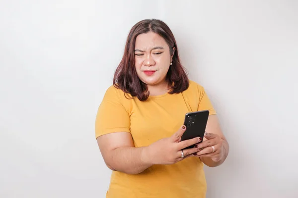白い背景に彼女の電話を保持しながら黄色のシャツに大きなサイズのアジアの女性の怒りと狂気の顔 — ストック写真