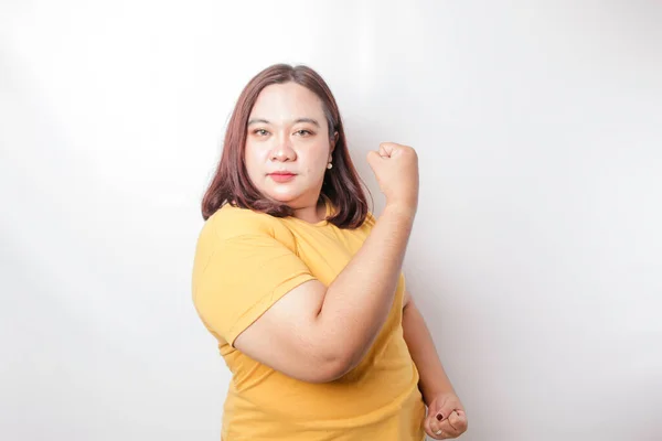 身穿黄色T恤的兴奋的亚洲大个子女人 高傲地举起胳膊和肌肉 做出了强有力的手势 — 图库照片