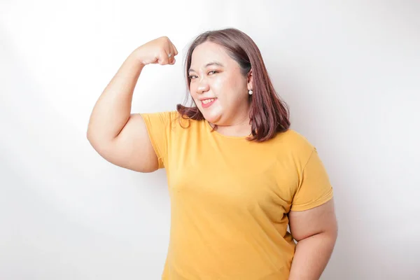흥분한 아시아의 덩치큰 여자가 티셔츠를 자랑스럽게 웃으며 근육을 치켜들며 몸짓을 — 스톡 사진