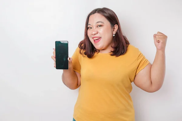 一位快乐的亚洲大个子女性在智能手机上挂着一副照片 照片上的她穿着一件黄色的衬衫 背景是白色的 — 图库照片
