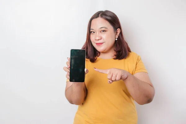 一位快乐的亚洲大个子女性在智能手机上挂着一副照片 照片上的她穿着一件黄色的衬衫 背景是白色的 — 图库照片