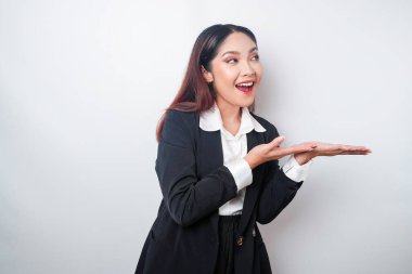 Heyecanlı Asyalı iş kadını siyah takım elbiseli, yanındaki fotokopi alanını işaret ediyor, beyaz arka planla izole edilmiş.