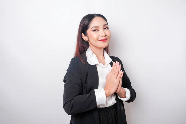 stock image A smiling young Asian woman employee wearing a black suit gestures a traditional greeting isolated over white background