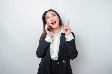 Heyecanlı Asyalı iş kadını, siyah takım elbiseli, beyaz arkaplan tarafından izole edilmiş bir telefon görüşmesi sırasında fotokopi odasını işaret ediyor.