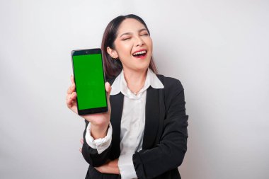 Mutlu genç bir iş kadını siyah takım elbise giyiyor, telefonunda beyaz arka planla izole edilmiş fotokopi alanı gösteriyor.