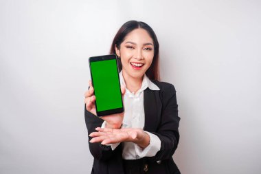 Mutlu genç bir iş kadını siyah takım elbise giyiyor, telefonunda beyaz arka planla izole edilmiş fotokopi alanı gösteriyor.
