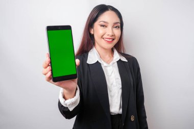 Mutlu genç bir iş kadını siyah takım elbise giyiyor, telefonunda beyaz arka planla izole edilmiş fotokopi alanı gösteriyor.