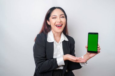 Mutlu genç bir iş kadını siyah takım elbise giyiyor, telefonunda beyaz arka planla izole edilmiş fotokopi alanı gösteriyor.