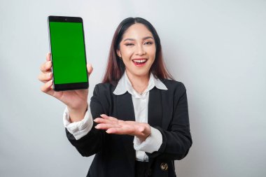 Mutlu genç bir iş kadını siyah takım elbise giyiyor, telefonunda beyaz arka planla izole edilmiş fotokopi alanı gösteriyor.