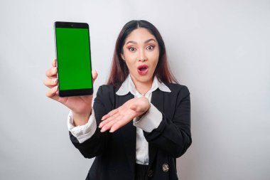 Siyah takım elbiseli Asyalı iş kadını akıllı telefonunda beyaz arka planla izole edilmiş fotokopi alanı gösteriyor.