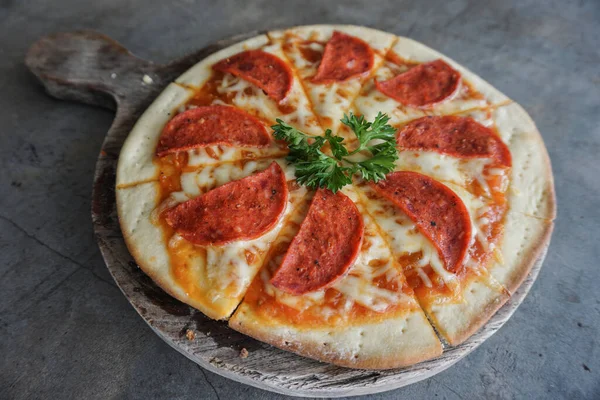A portrait of a tasty pepperoni pizza on a wooden pan isolated by grey concrete background