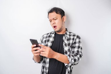 Tatmin olmamış Asyalı bir adam, elinde telefonuyla asfalt gömlek giymiş asabi bir yüz ifadesi takınıyor.