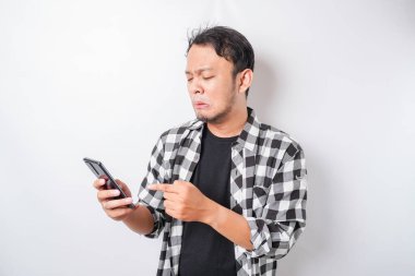 Tatmin olmamış Asyalı bir adam, elinde telefonuyla asfalt gömlek giymiş asabi bir yüz ifadesi takınıyor.