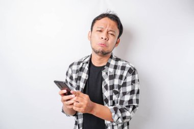 Tatmin olmamış Asyalı bir adam, elinde telefonuyla asfalt gömlek giymiş asabi bir yüz ifadesi takınıyor.