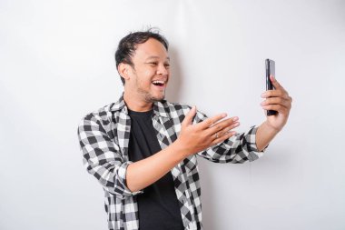 Asyalı mutlu bir adamın portresi beyaz arka planla izole edilmiş telefonunu tutarken gülümsüyor.