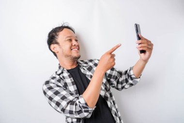 Asyalı mutlu bir adamın portresi beyaz arka planla izole edilmiş telefonunu tutarken gülümsüyor.