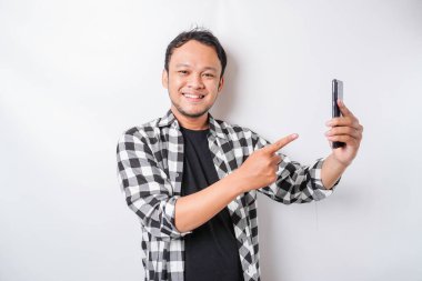 Asyalı mutlu bir adamın portresi beyaz arka planla izole edilmiş telefonunu tutarken gülümsüyor.