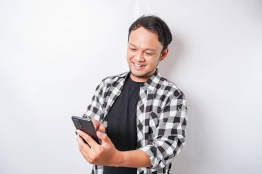 Asyalı mutlu bir adamın portresi beyaz arka planla izole edilmiş telefonunu tutarken gülümsüyor.