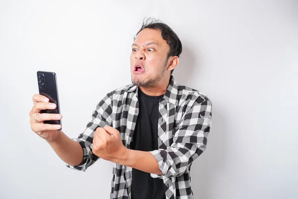 白地に携帯電話を持ちながらタータンシャツを着たアジア人男性の怒りと狂気の顔 — ストック写真