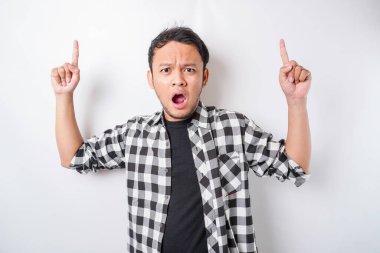Şok olmuş Asyalı adam, beyaz bir arka planla izole edilmiş, üzerindeki fotokopi alanını işaret ediyor.