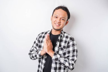 Asyalı gülümseyen genç bir adam, beyaz arka planda izole edilmiş geleneksel selamlaşmaları işaret ediyor.