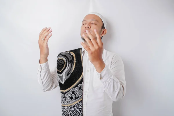 Happy handsome Asian Muslim man with prayer rug on his shoulder is praying to God.
