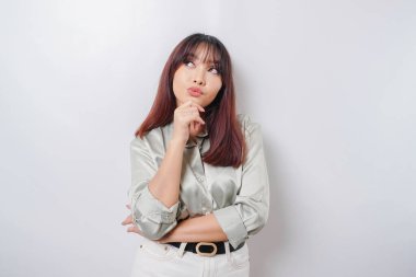 Düşünceli genç bir kadın yeşil bir gömlek giyiyor ve çenesini beyaz arka planda tutuyor.