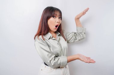 Beyaz arka planla izole edilmiş, yanındaki fotokopi alanını gösteren yeşil tişörtlü, şok olmuş Asyalı kadın.