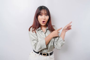 Beyaz arka planla izole edilmiş, yanındaki fotokopi alanını gösteren yeşil tişörtlü, şok olmuş Asyalı kadın.