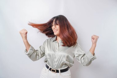 Mutlu ve başarılı bir yüzü olan genç bir Asyalı kadın, beyaz arka planla izole edilmiş adaçayı rengi yeşil gömlek giyiyor.