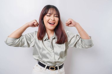 Heyecanlı Asyalı kadın, yeşil bir gömlek giyiyor. Kollarını ve kaslarını gururla kaldırarak güçlü bir hareket sergiliyor.