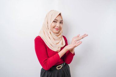 Heyecanlı Asyalı kadın tesettürlü, yanındaki fotokopi alanını işaret ediyor, beyaz arka planla izole edilmiş.