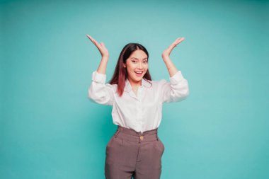 Telaşlı Asyalı kadın beyaz gömlekli, üstündeki fotokopi alanını işaret ediyor, mavi arka planla izole edilmiş.