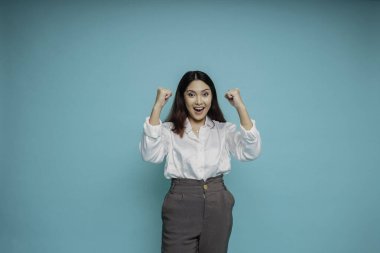 Mutlu ve başarılı bir yüzü olan, mavi arka planda beyaz gömlek giyen genç bir Asyalı kadın.