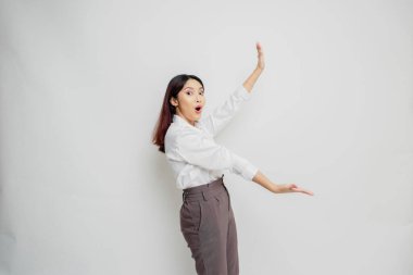 Beyaz gömlekli, beyaz tişörtlü, beyaz arkaplan tarafından izole edilmiş, yanındaki fotokopi alanını gösteren Asyalı kadın şok oldu.