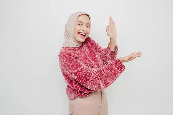 兴奋的亚洲穆斯林女人穿着粉色毛衣 头戴头巾 指着旁边被白色背景隔开的抄袭空间 — 图库照片