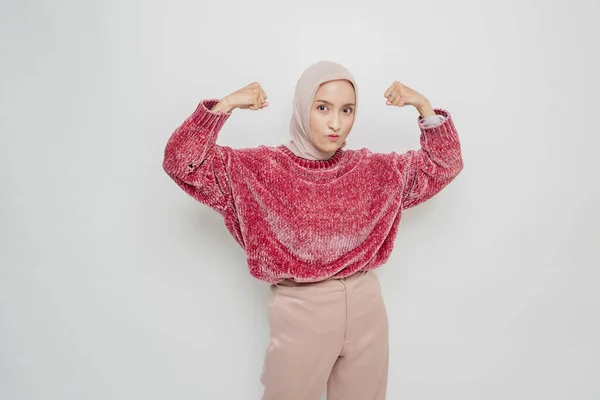 興奮アジアのイスラム教徒の女性はピンクのセーターとヒジャーブを着て 彼女の腕と筋肉を誇らしげに笑顔持ち上げることによって強いジェスチャーを示しています — ストック写真
