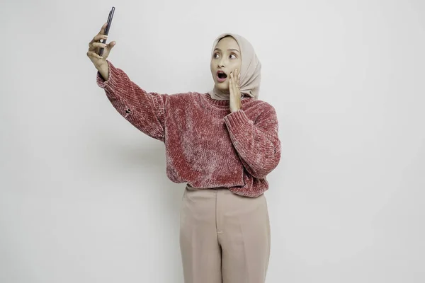Zszokowana Azjatka Różowym Swetrze Hidżabie Trzymająca Telefon Odizolowana Białym Tłem — Zdjęcie stockowe
