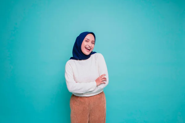自信に満ちた笑顔の肖像白いシャツを着たアジア系ムスリム女性と腕を組んで立つヒジャーブ 青い背景の上に孤立したカメラを見る — ストック写真