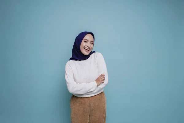 自信に満ちた笑顔の肖像白いシャツを着たアジア系ムスリム女性と腕を組んで立つヒジャーブ 青い背景の上に孤立したカメラを見る — ストック写真