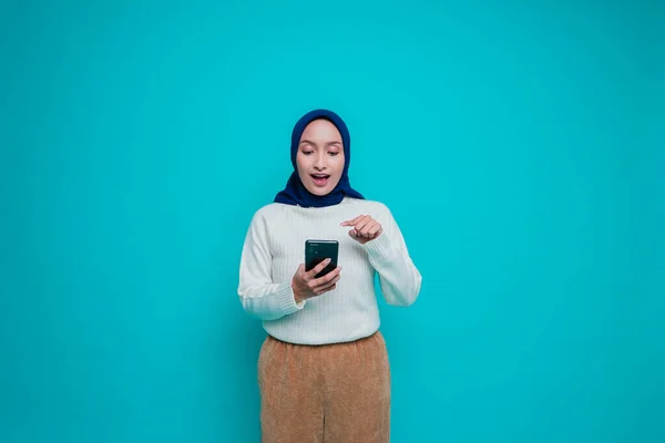 Потрясенная Азиатка Белой Рубашке Хиджабе Держащая Телефон Изолированная Синим Фоном — стоковое фото