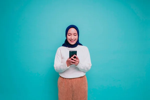 一个身穿白衬衫 头戴头巾 拿着手机 被蓝色背景隔离的快乐的亚洲穆斯林妇女的肖像 — 图库照片