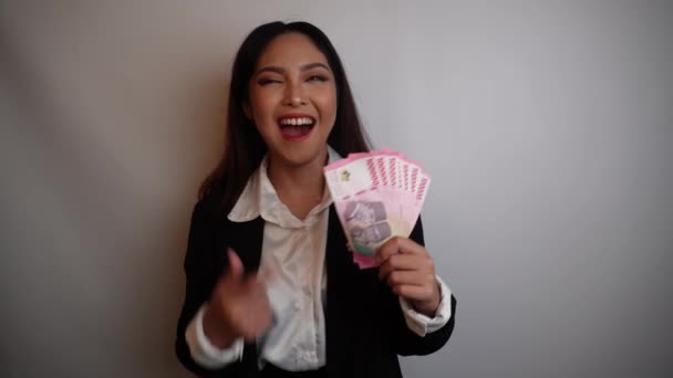 一位快乐的年轻女商人身穿黑色西服 手里拿着印尼盾的现金 这些钱与白人背景无关 — 图库视频影像