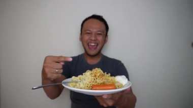 Genç Asyalı adam mutlu ve heyecanlı bir ifadeyle hazır erişte yiyor.