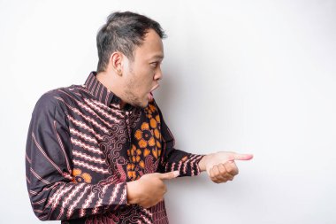 Beyaz arka planla izole edilmiş, yanındaki fotokopi odasını gösteren batik tişörtlü, şok olmuş Asyalı adam.