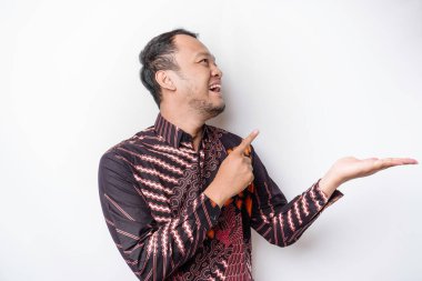 Batik tişört giyen heyecanlı Asyalı adam yanındaki fotokopi odasını işaret ediyor, beyaz arka planla izole edilmiş.