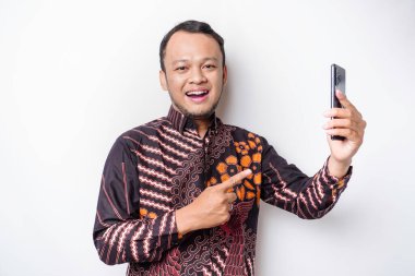 Batik gömlek giyen ve telefonunu beyaz arka planda tutan mutlu Asyalı bir adamın portresi.