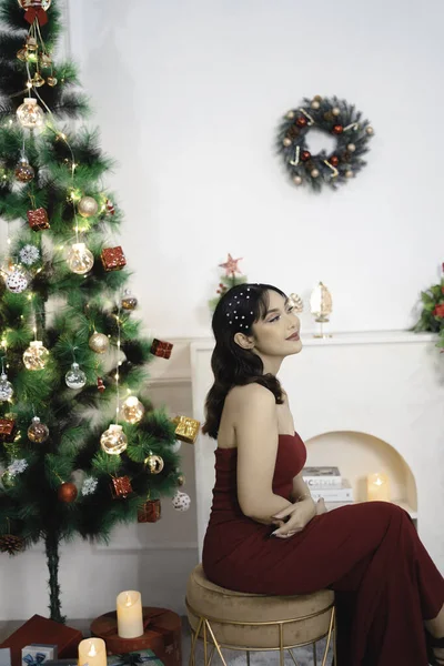 かなり若い女の子の肖像居心地の良い座って 笑顔装飾されたクリスマスのリビングルームで赤いガウンを身に着けて室内 — ストック写真
