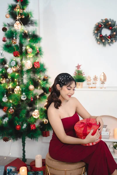 かなり若い女の子居心地の良いの肖像は クリスマスプレゼントを保持ダウン座って 室内装飾されたクリスマスのリビングルームで赤いガウンを身に着けて笑顔 — ストック写真