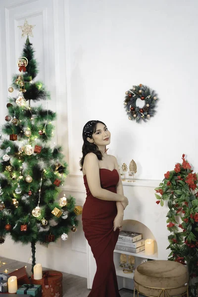赤いガウンを着たかなり若い女の子の肖像画 カメラで笑顔 室内装飾されたクリスマスのリビングルームに立って — ストック写真